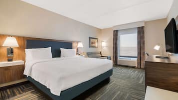 A hotel room with a large bed, two bedside tables with lamps, a desk with a television, and a large window with curtains.