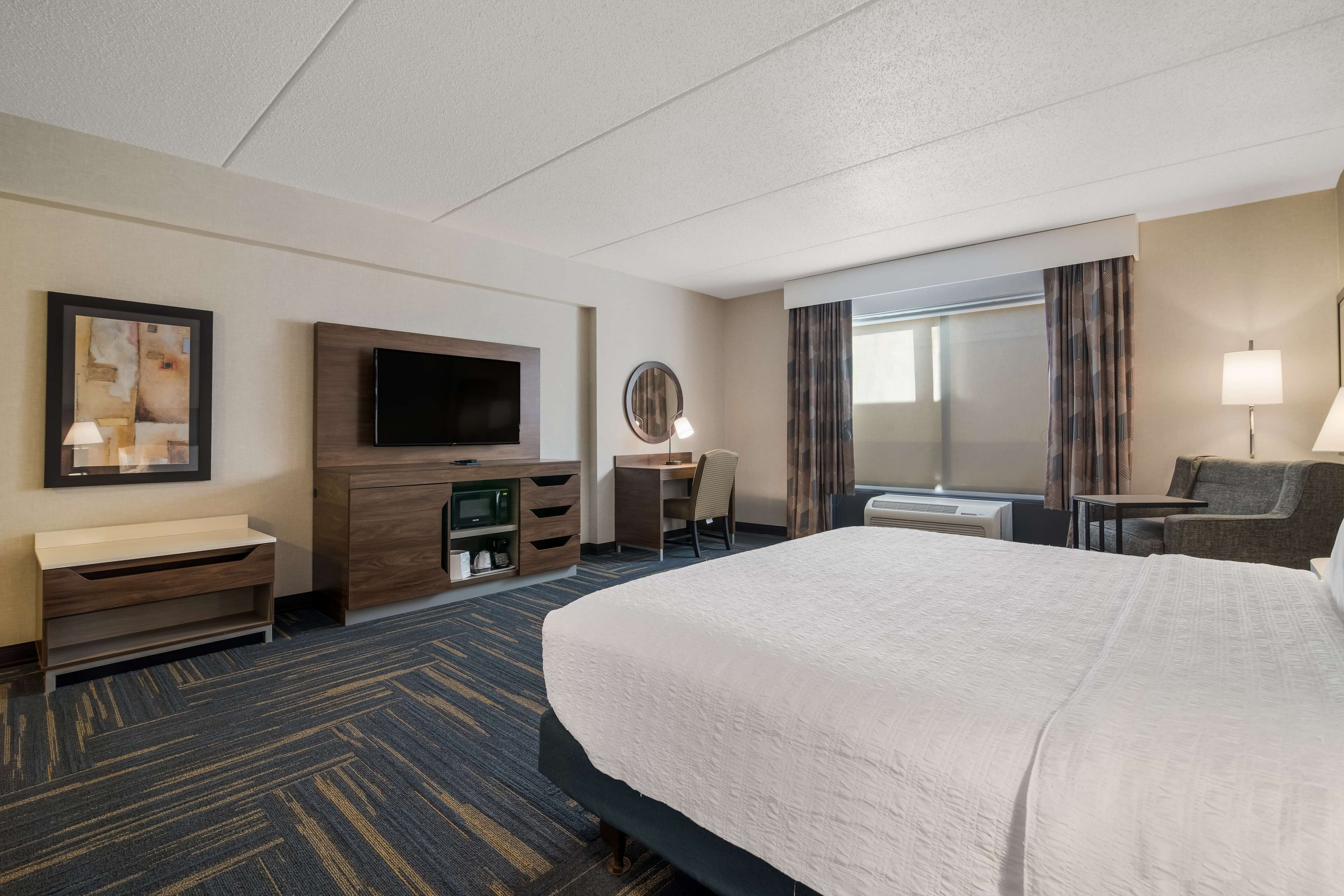A hotel room with a large bed, a desk, a television, a mirror, and a window with curtains.