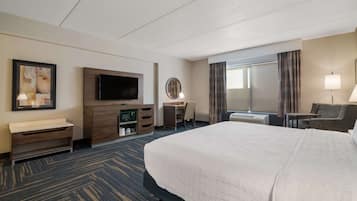 A hotel room with a large bed, a desk, a television, a mirror, and a window with curtains.