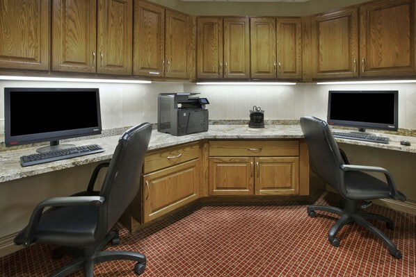 A kitchen with wooden cabinets, two computer workstations, and a tiled floor.