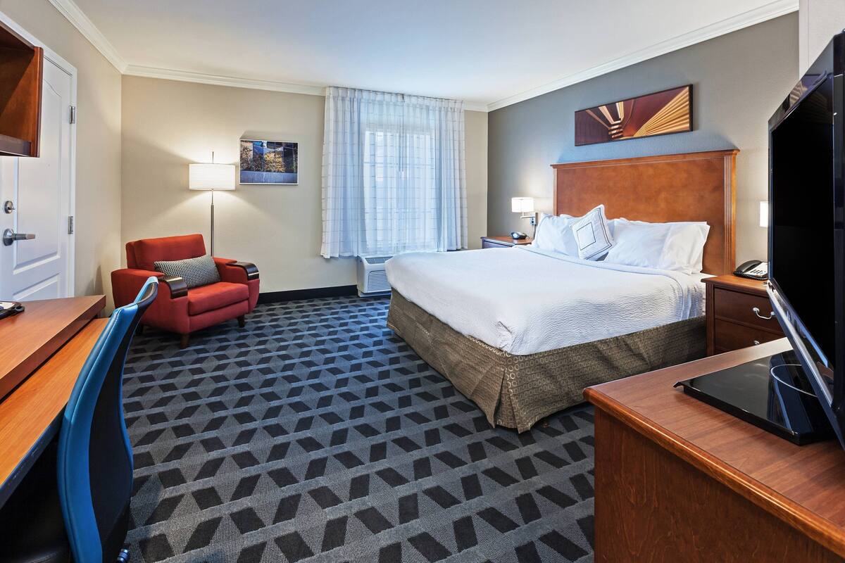 A hotel room with a bed, a desk, a chair, a TV, and a window with curtains.