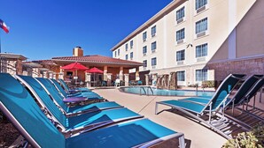Un espace piscine avec des chaises longues et un bâtiment doté de nombreuses fenêtres et d’un toit rouge.