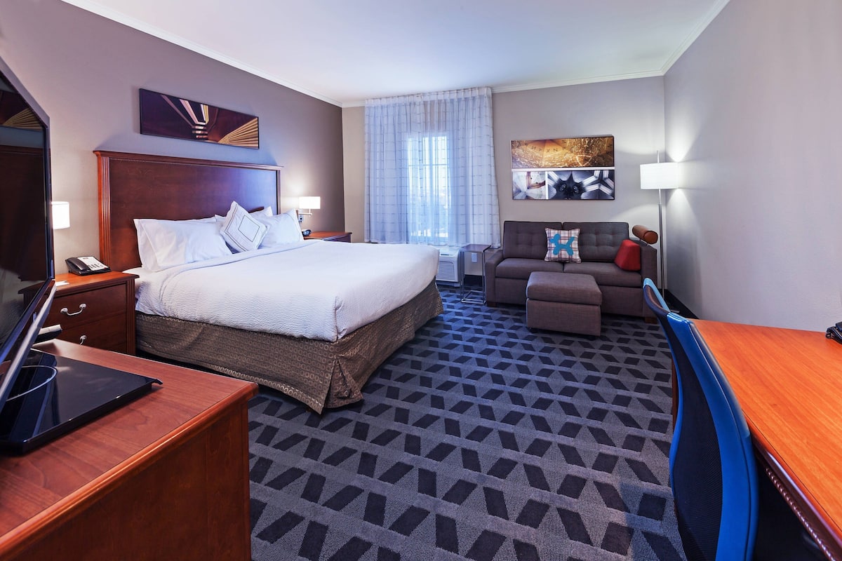 A hotel room with a large bed, a desk, a chair, a sofa, and a TV.