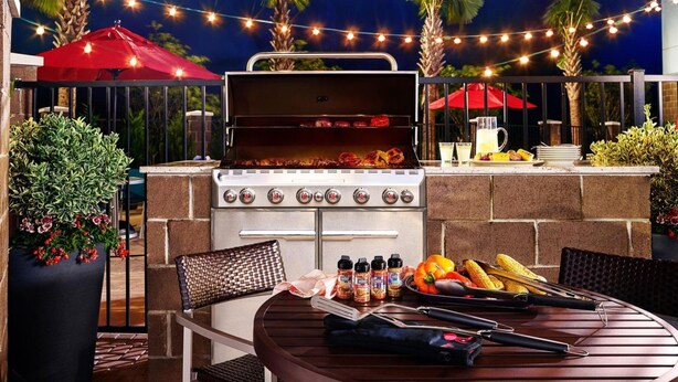 Un espace barbecue extérieur équipé d’un gril, de sièges et de guirlandes lumineuses.