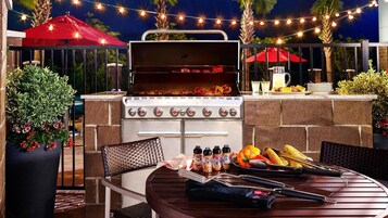Zona de barbacoa al aire libre con parrilla, asientos e iluminación con luces colgantes.