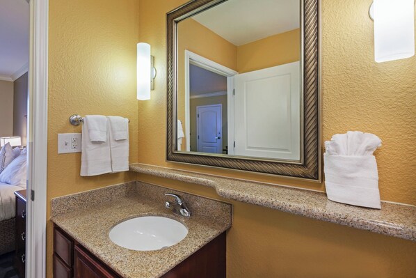 A bathroom with a granite countertop sink, a large mirror, and two towels hanging on the wall.