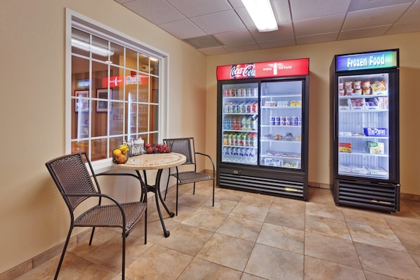Un área de estar con una mesa y sillas, un refrigerador de Coca-Cola y un refrigerador para alimentos congelados.