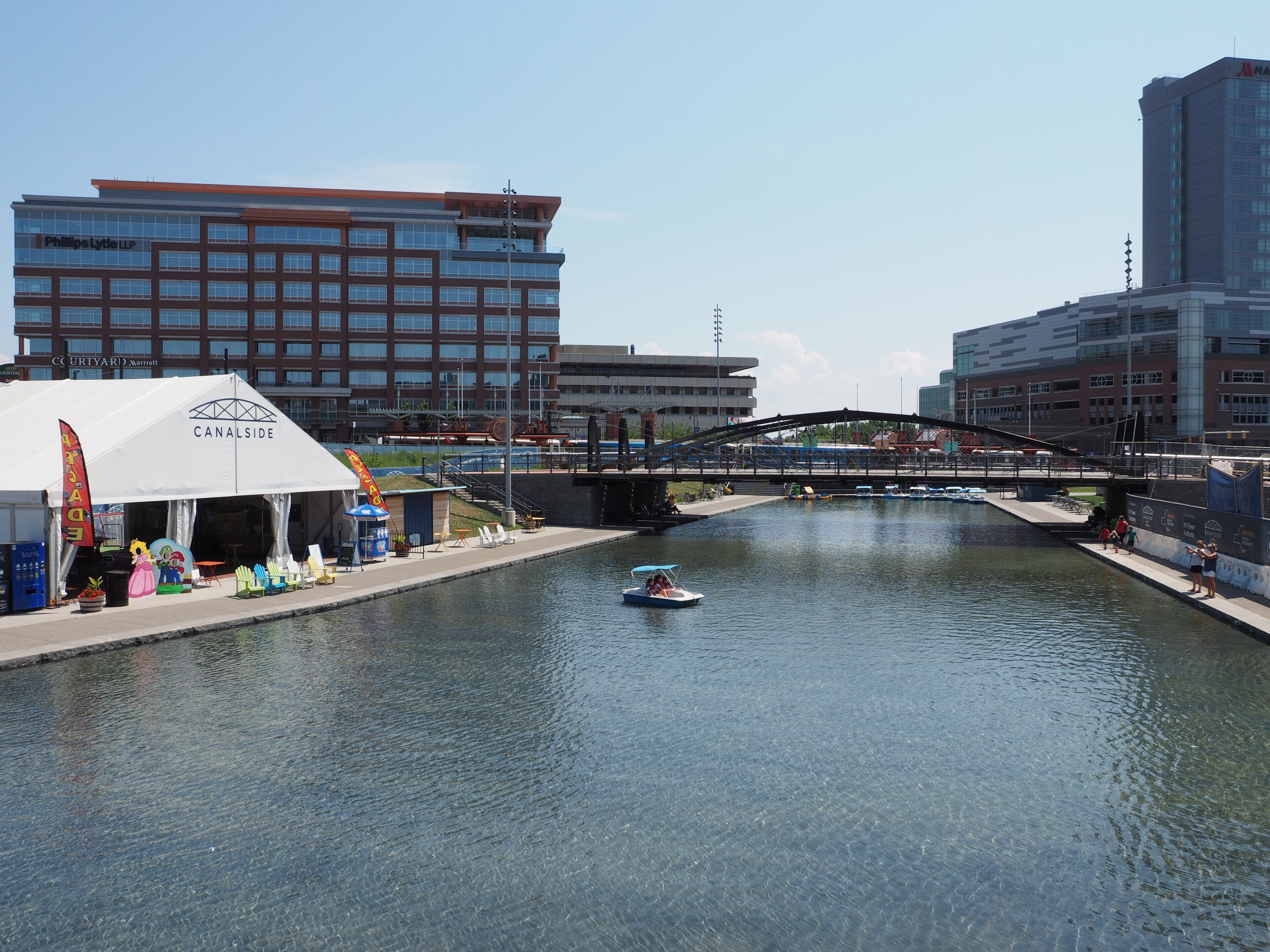 Un canal amb un vaixell, una tenda blanca i edificis moderns al fons.