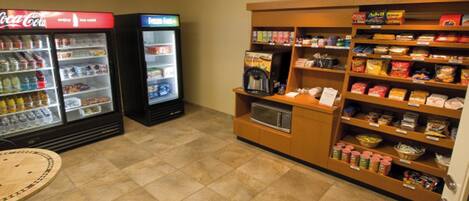 A vending area with Coca-Cola and frozen food machines, a microwave, and shelves stocked with snacks and beverages.