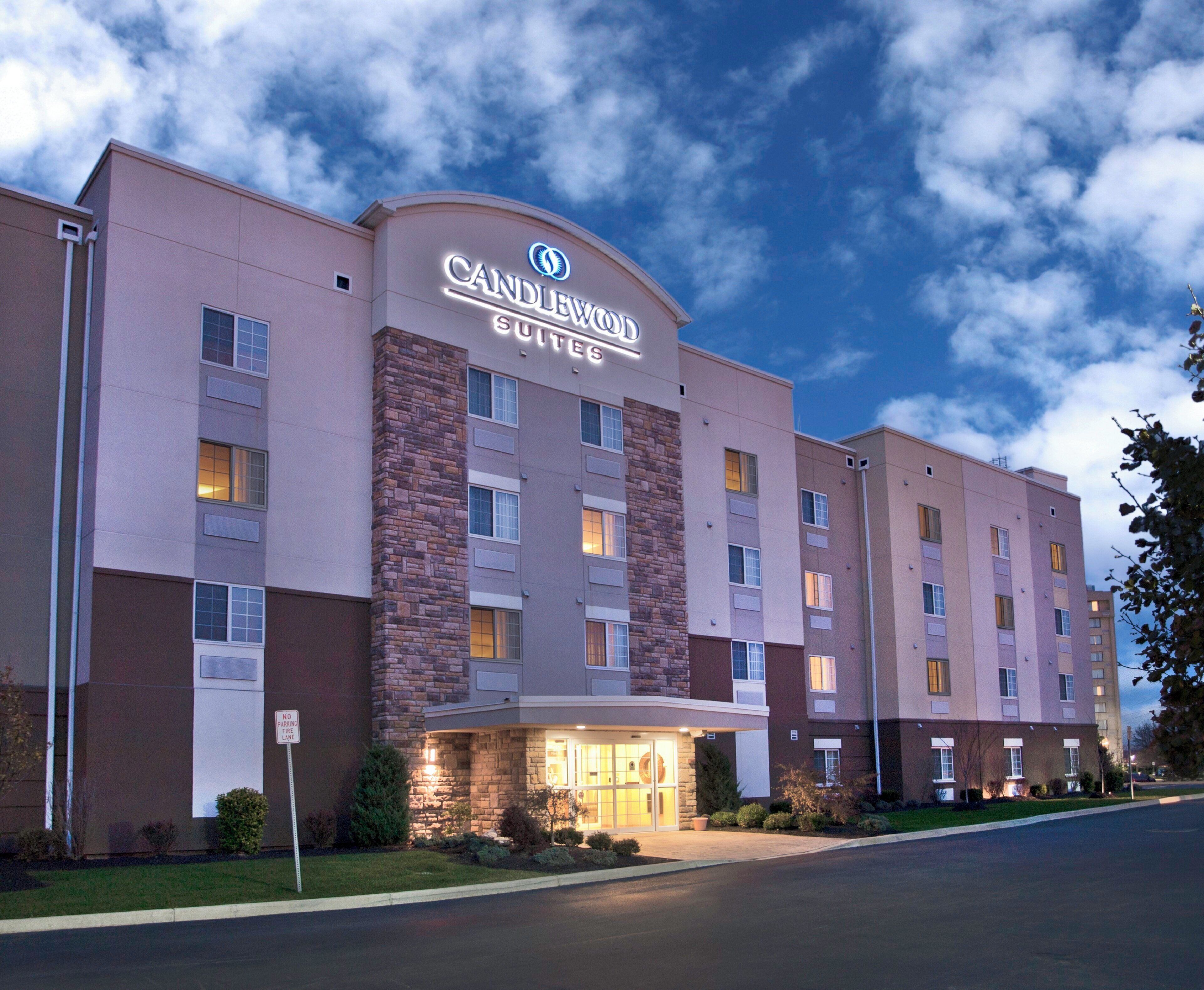 A multi-story hotel with a prominent 'Candlewood Suites' sign, a brick facade, and a well-lit entrance.