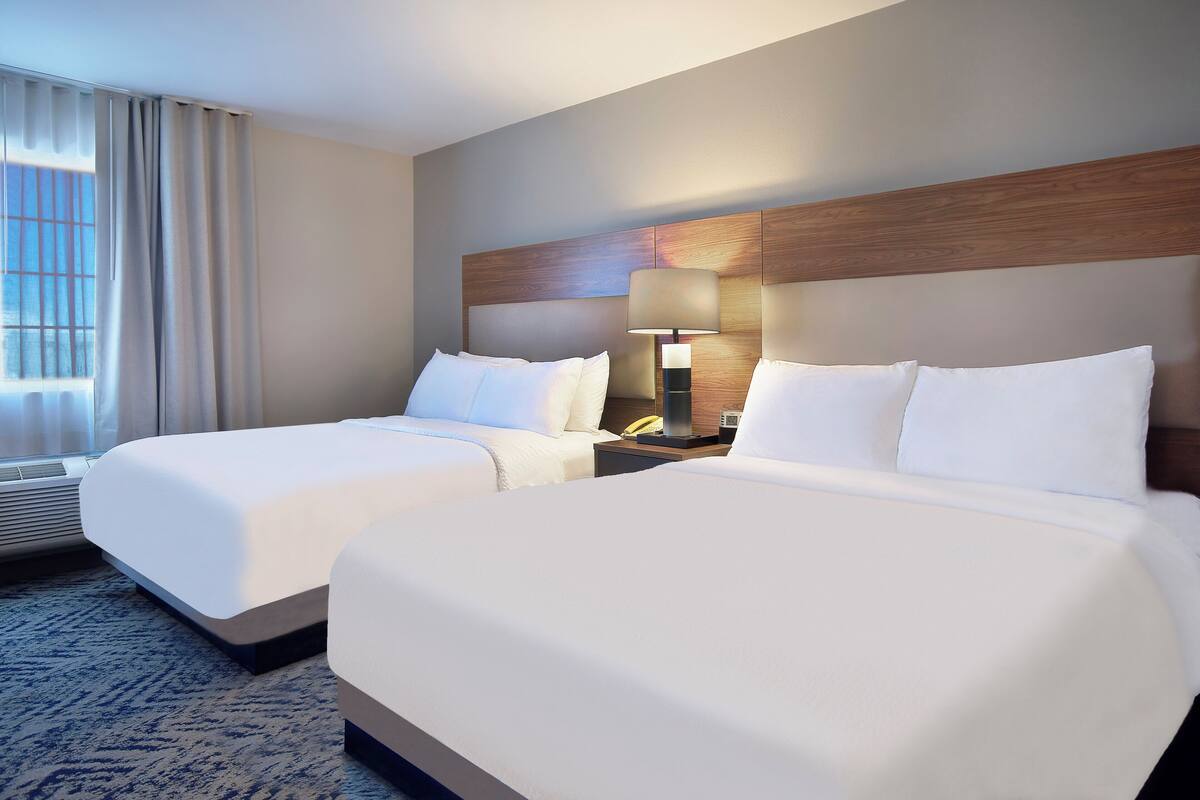 Een hotelkamer met twee bedden, een houten hoofdeinde, een nachtkastje met een lamp en een raam met gordijnen.