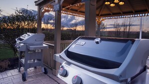 Un espace barbecue extérieur doté d’un thermomètre intégré et de boutons de réglage, situé sous un pavillon couvert illuminé de guirlandes lumineuses.