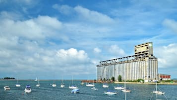 Un gran edificio industrial con varias estructuras cilíndricas, rodeado de agua tranquila y varias embarcaciones pequeñas.