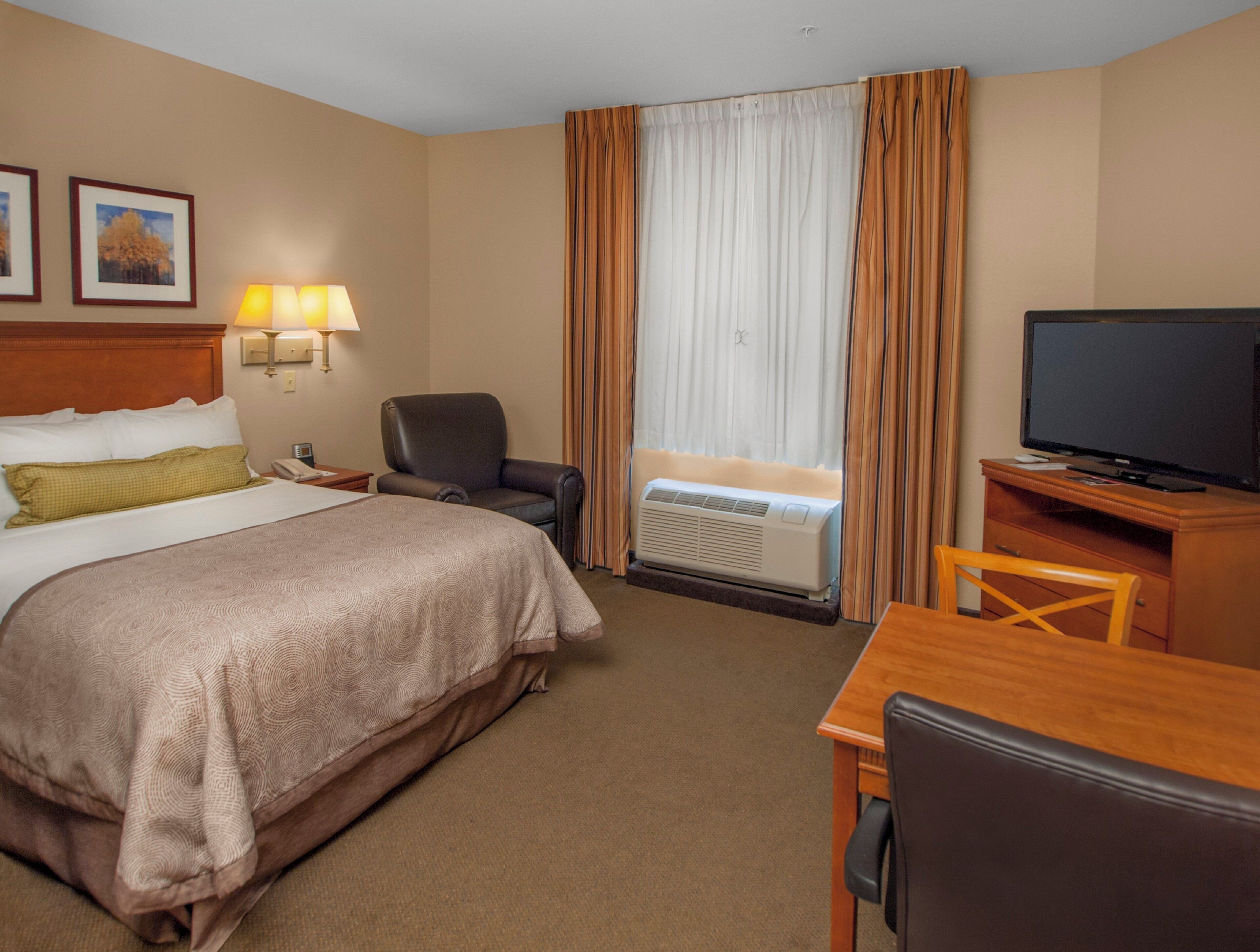 A hotel room with a bed, a desk, a chair, a television, an air conditioning unit, and curtains.