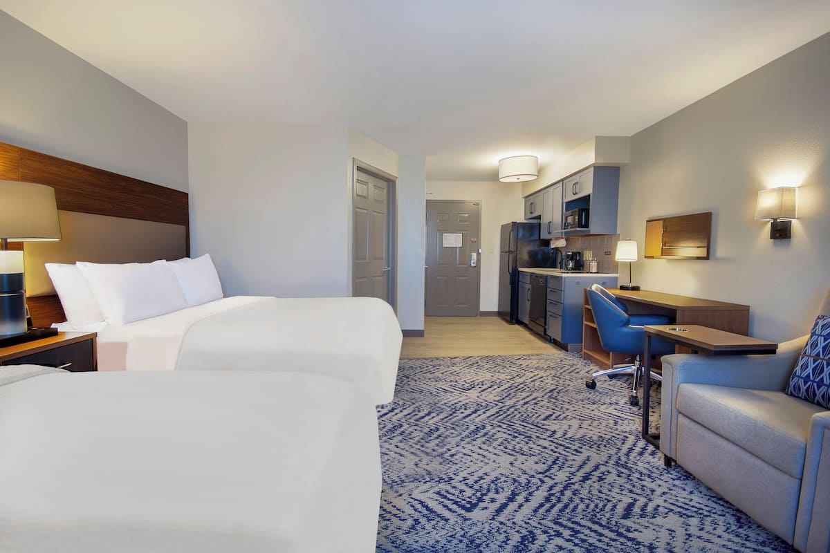 Een hotelkamer met twee bedden, een bureau, een stoel, een kitchenette en een badkamer.