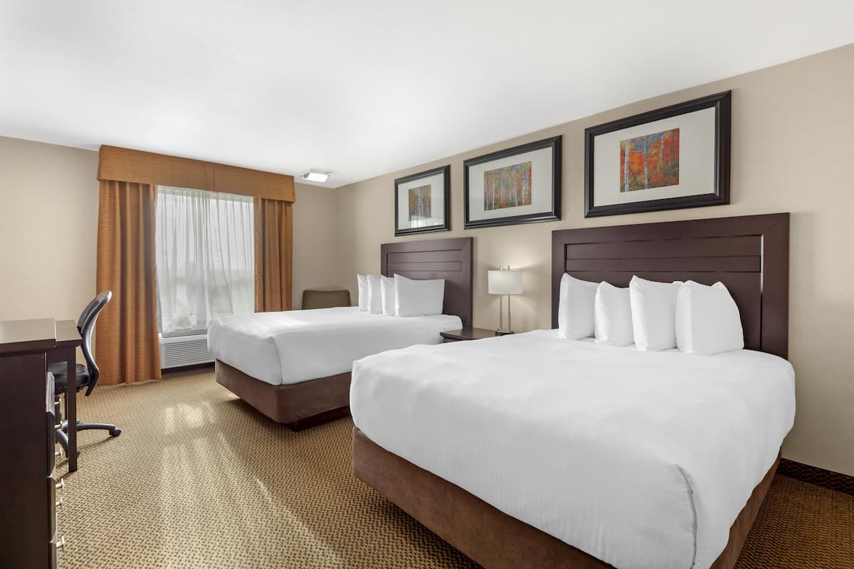 Une chambre d’hôtel avec deux lits, un bureau, une chaise et une grande fenêtre avec des rideaux.