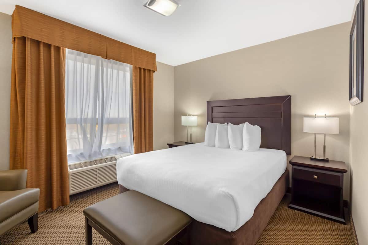 Une chambre d’hôtel avec un grand lit, une table de chevet avec une lampe, une chaise et une fenêtre avec des rideaux.