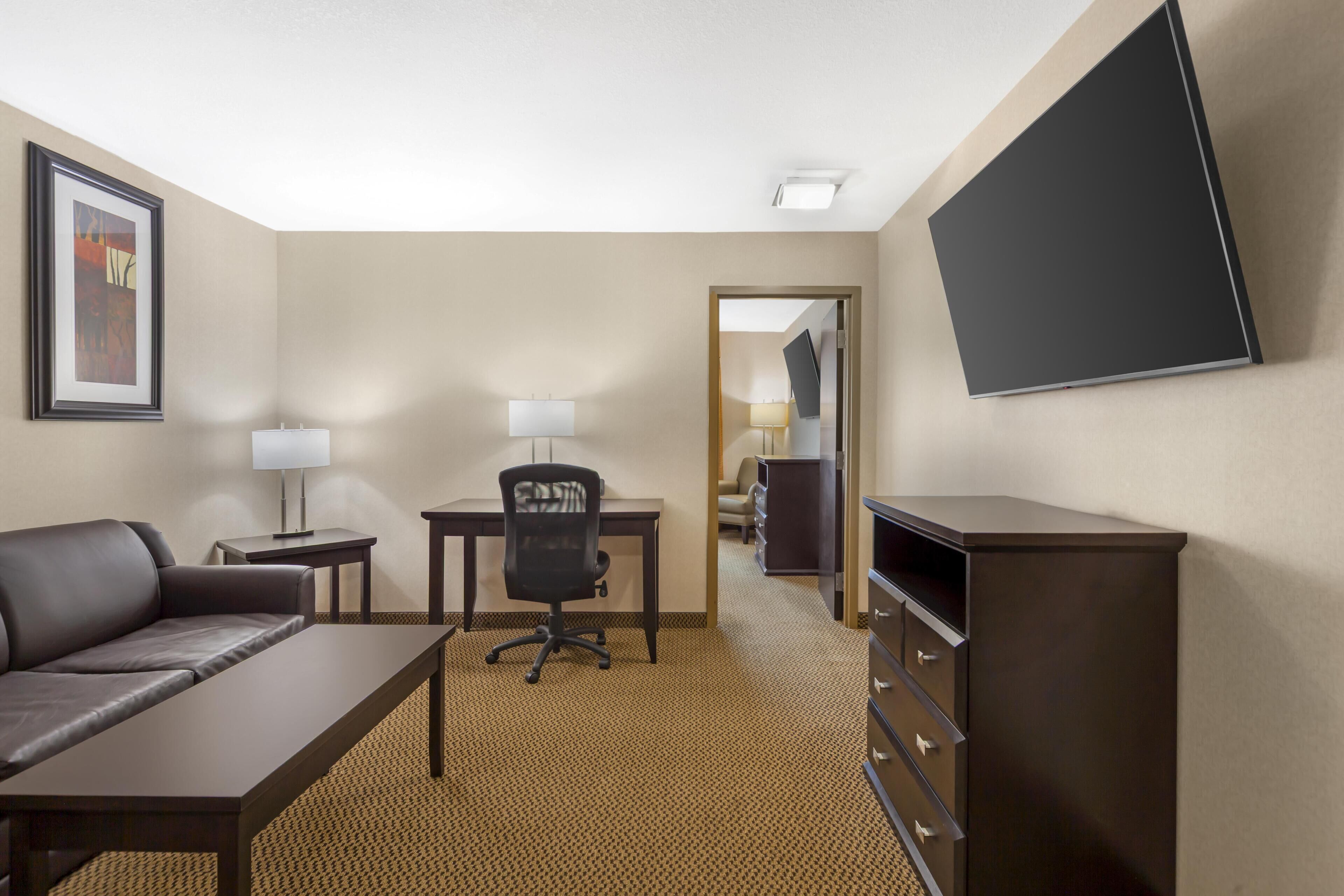 Habitación de hotel con sofá, escritorio, silla, televisor, lámpara y cómoda.
