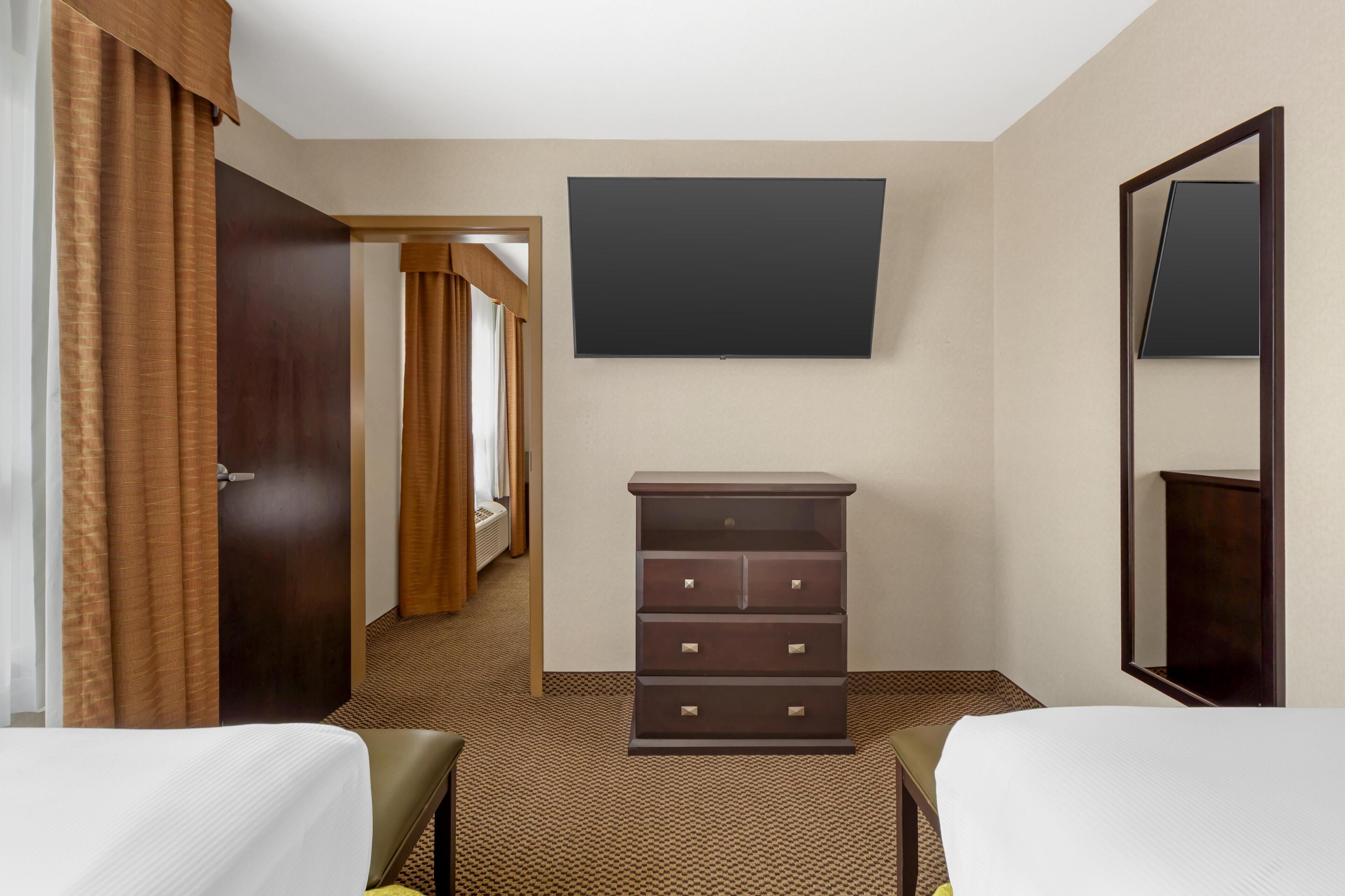 A hotel room with two beds, a dresser, a flat-screen TV, and a mirror.