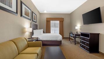 Una habitación de hotel con una cama, un sofá, un escritorio, un televisor y cuadros en la pared.
