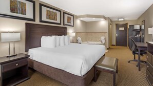 Habitación de hotel con una cama grande, un escritorio, una silla, un baño con bañera y obras de arte en las paredes.