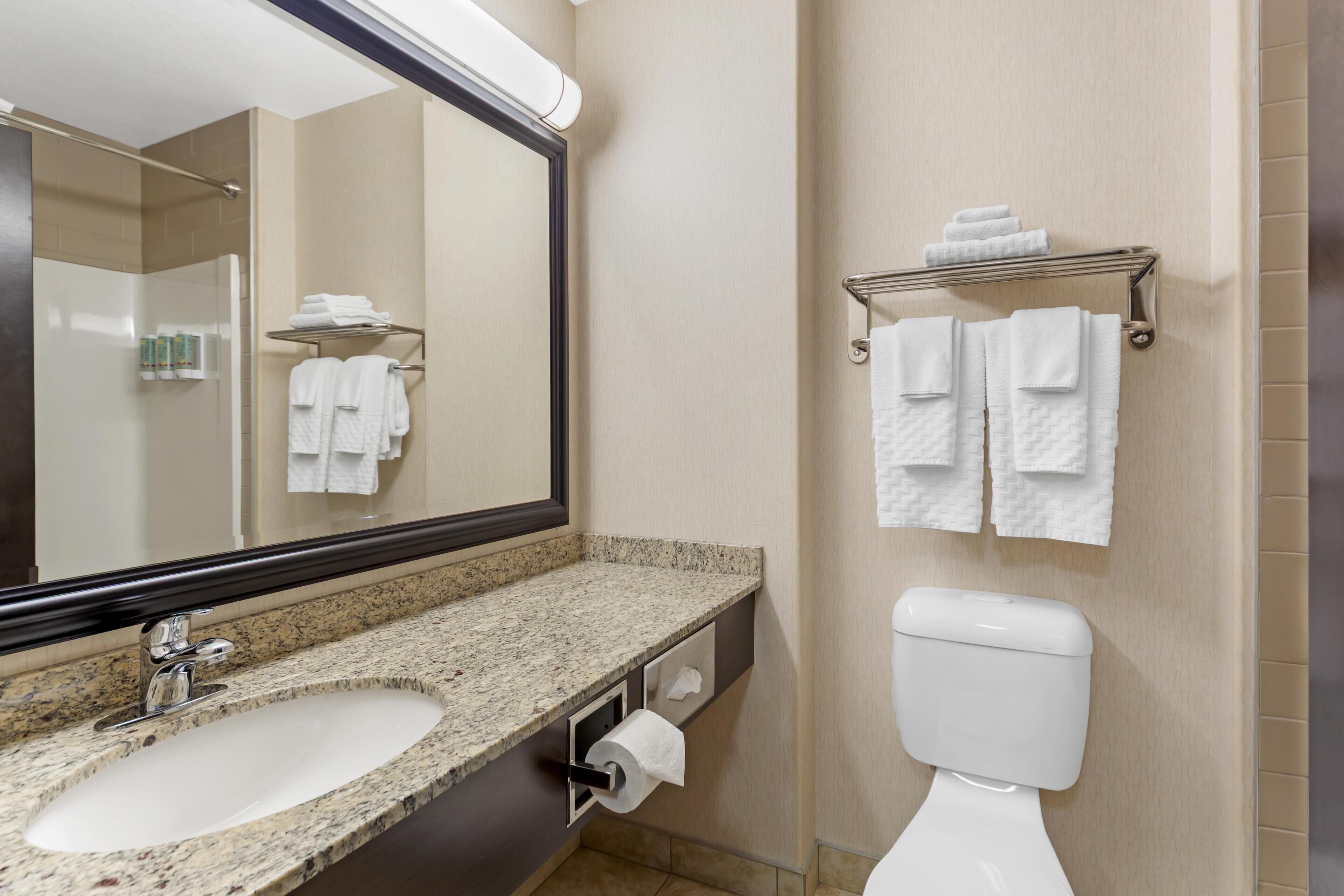 A bathroom with a granite countertop sink, a toilet, and a towel rack with folded towels.