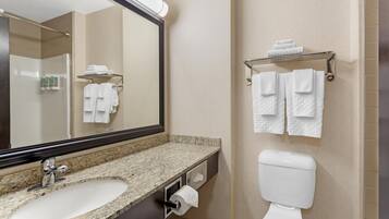 A bathroom with a granite countertop sink, a toilet, and a towel rack with folded towels.