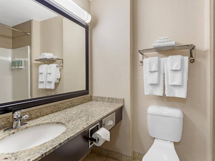 A bathroom with a granite countertop sink, a toilet, and a towel rack with folded towels.