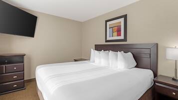 Une chambre d’hôtel avec un grand lit, une commode, une table de chevet, une lampe et un téléviseur à écran plat fixé au mur.