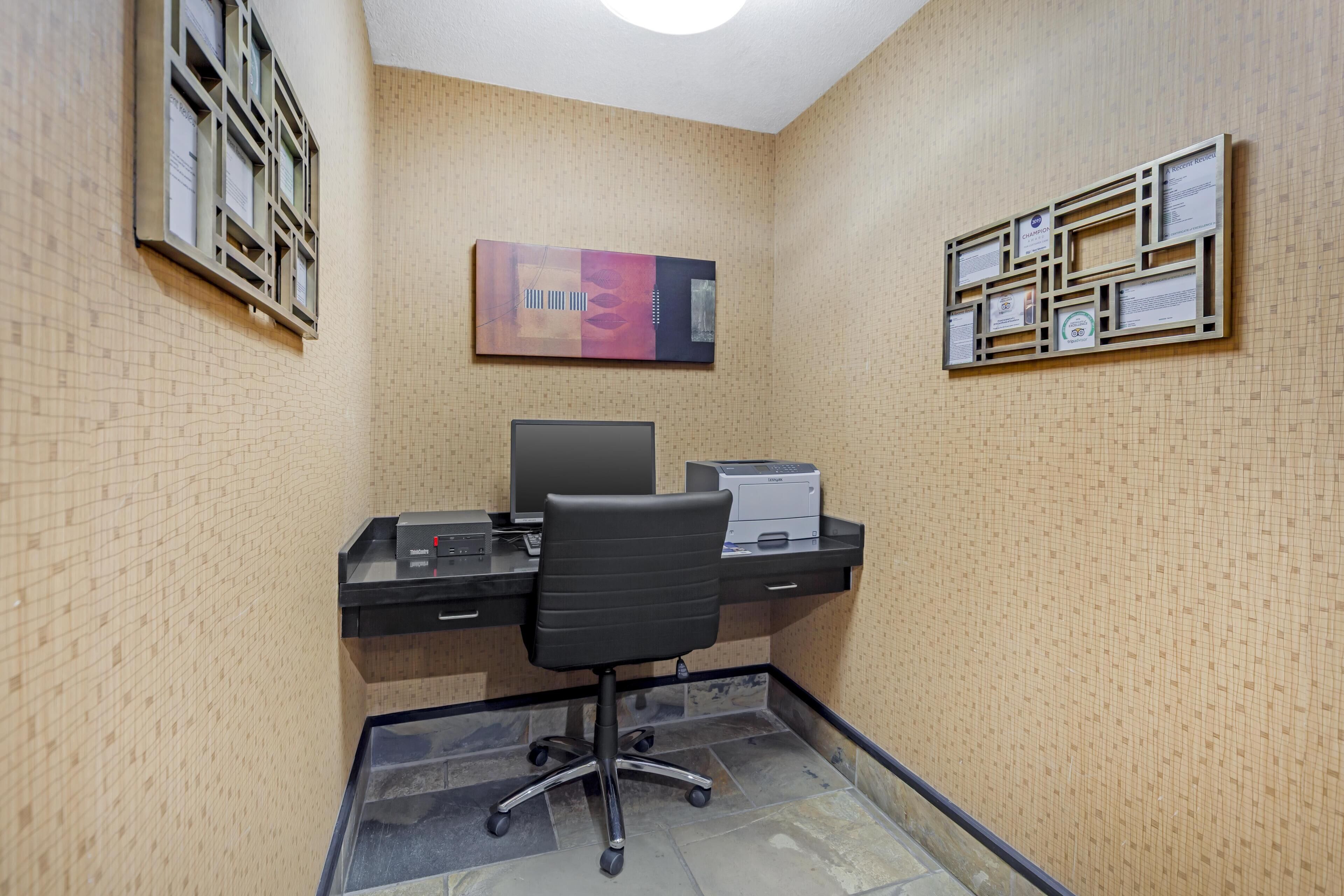 A small office with a desk, chair, computer, and printer. There are certificates on the wall.