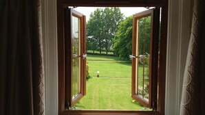 Une fenêtre ouverte donnant sur une pelouse bien entretenue et des arbres.