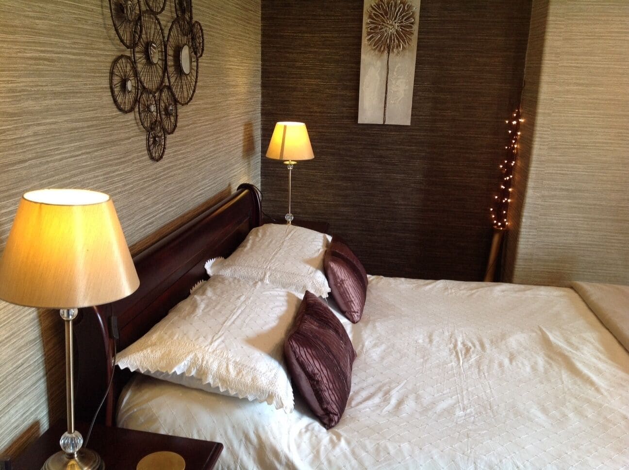 A neatly made bed with white linens and two decorative pillows, a bedside lamp, and a wall art piece.