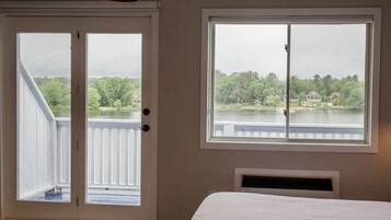 Un dormitorio con una cama grande, un ventanal con vistas a un lago y casas, y una puerta que da a un balcón exterior.