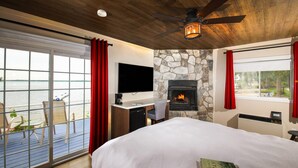 Ein Schlafzimmer mit einem großen Bett, einem Kamin, einem Fernseher und einem Balkon mit Blick aufs Wasser.