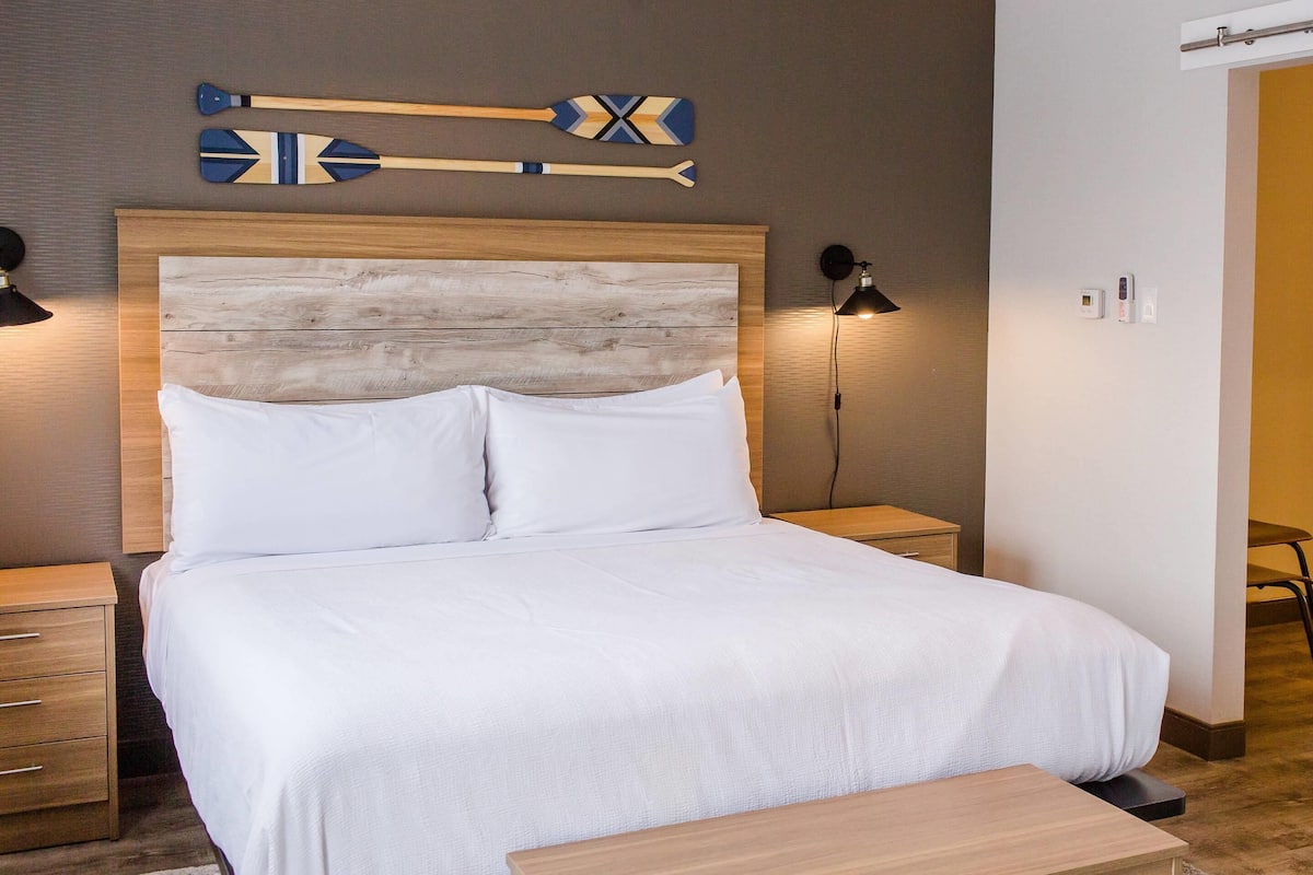 A neatly made bed with white linens, a wooden headboard, and two bedside tables with lamps.