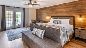 Ein Schlafzimmer mit einem großen Bett, einem Deckenventilator, einem Holzkopfteil, zwei Nachttischen und Blick durch eine Glastür.