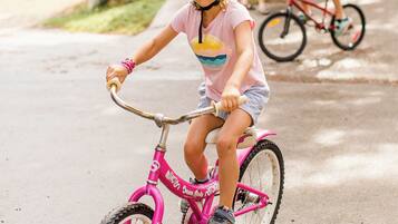 Un nen o nena pedaleja amb una bicicleta rosa sobre un camí pavimentat.