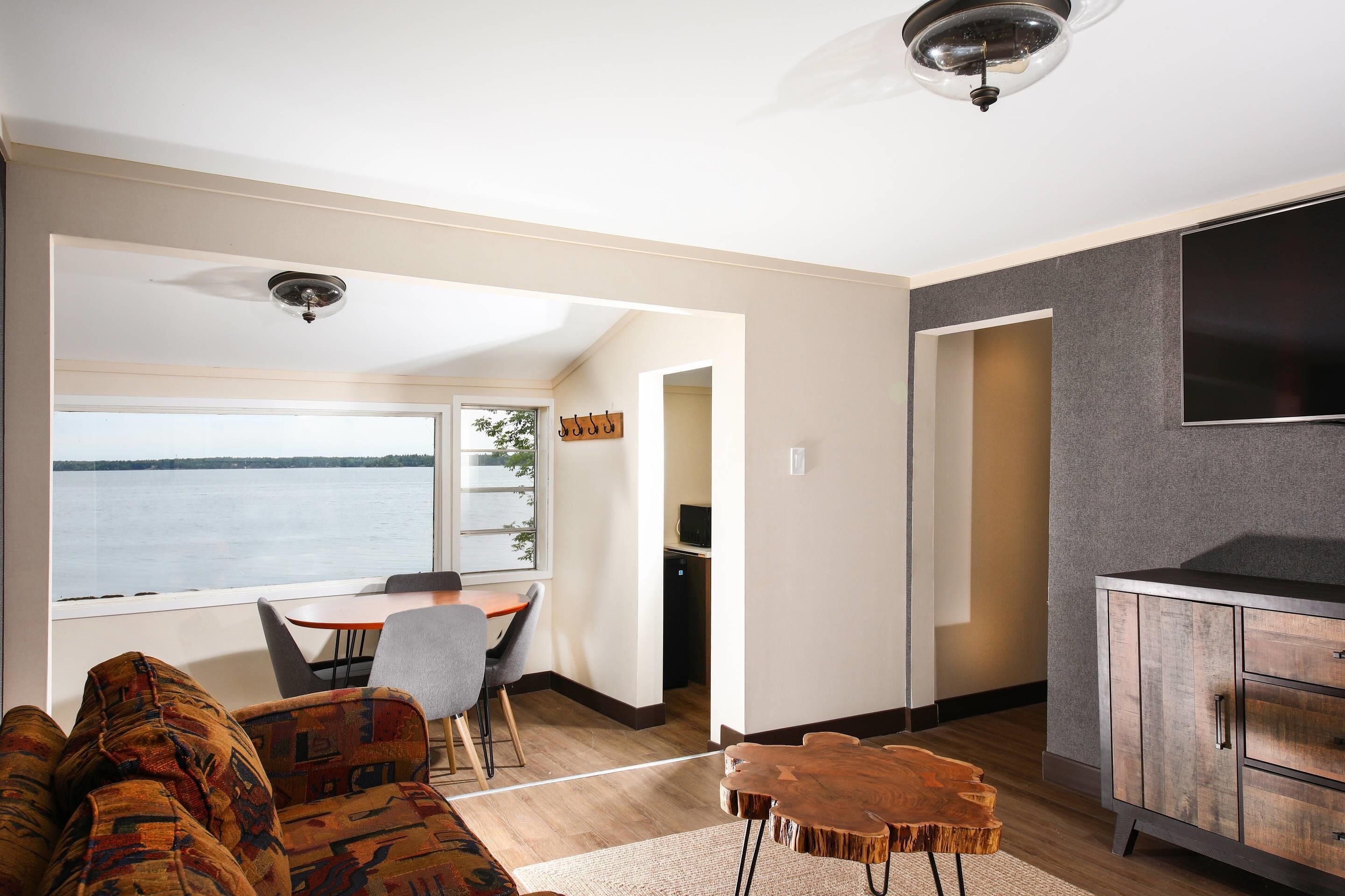 A modern living room with a view of the water, a dining area, and a kitchen with a TV.