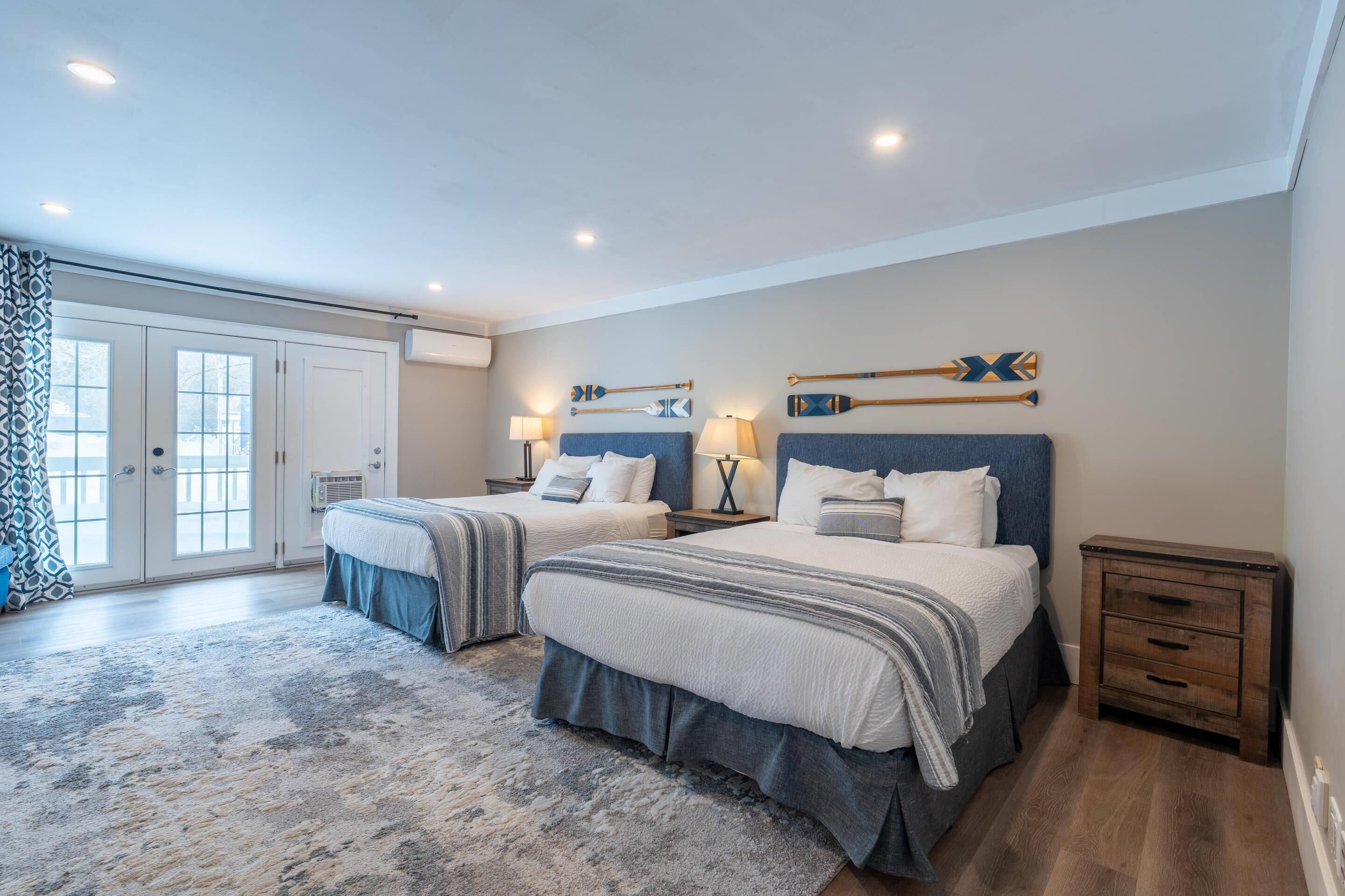A bedroom with two beds, a large window, and a wooden nightstand.