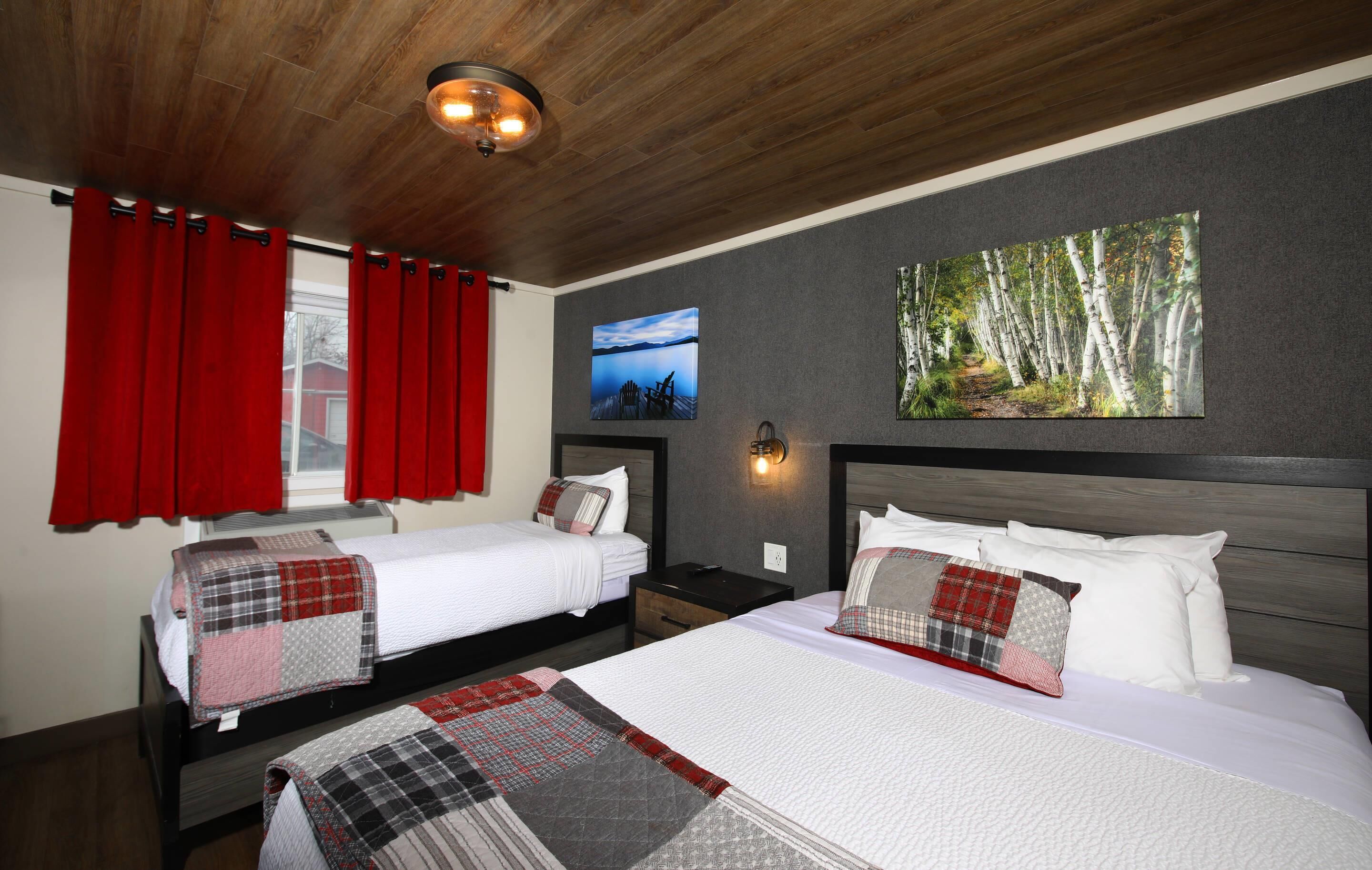 Quarto de hotel com duas camas, cortinas vermelhas, uma grande pintura com tema de floresta e uma imagem do céu noturno na parede.