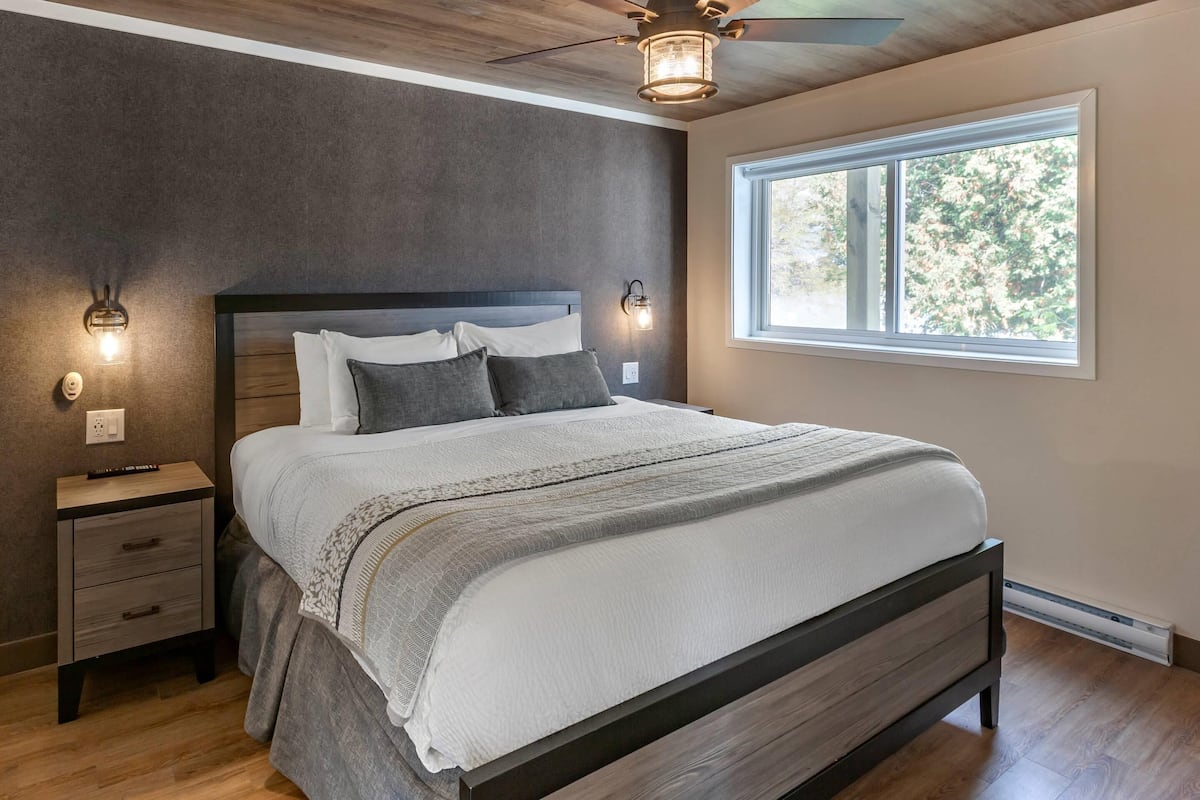 A bedroom with a bed, nightstands, wall sconces, a ceiling fan, and a window.