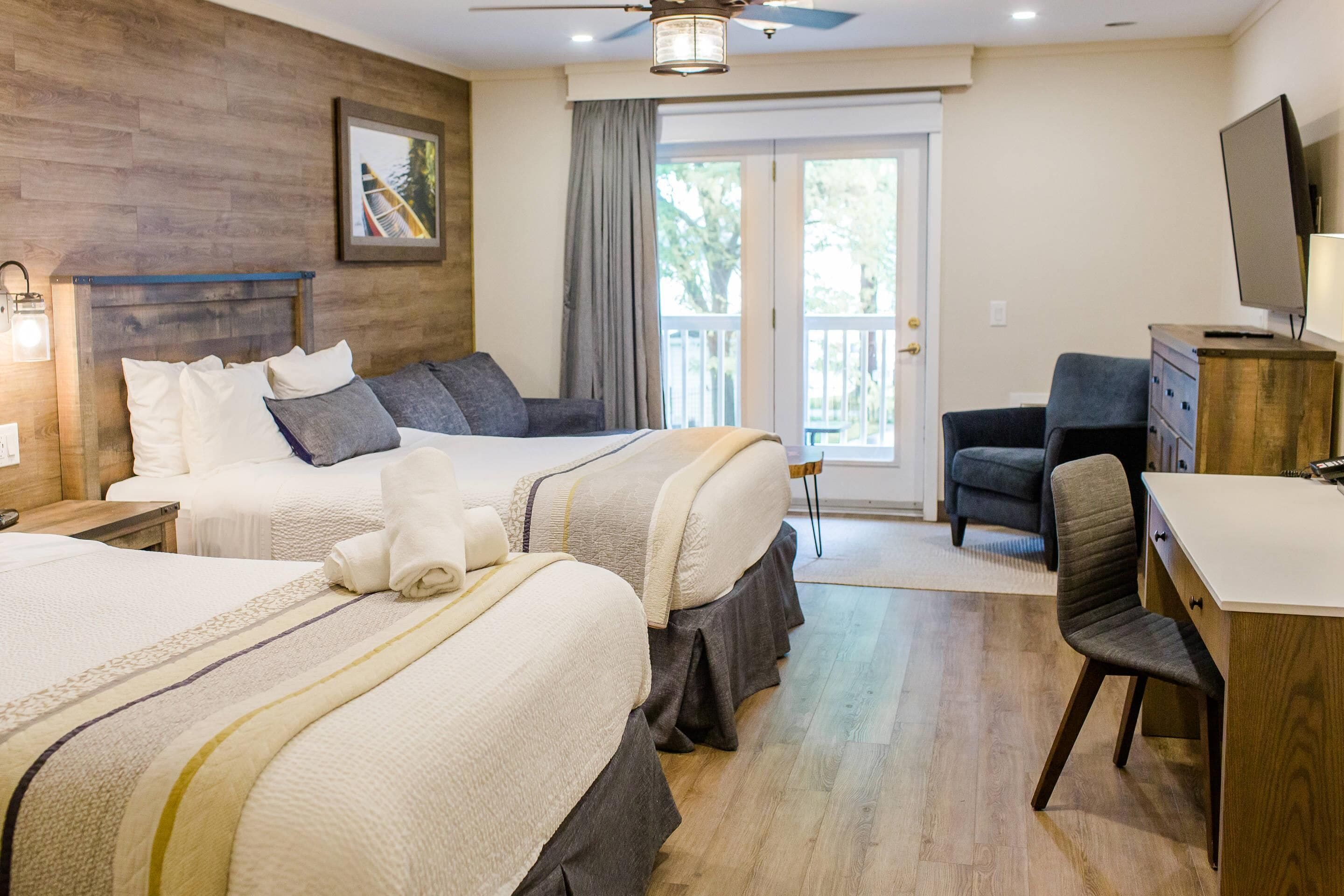 A hotel room with two beds, a desk, a chair, a television, and a balcony.