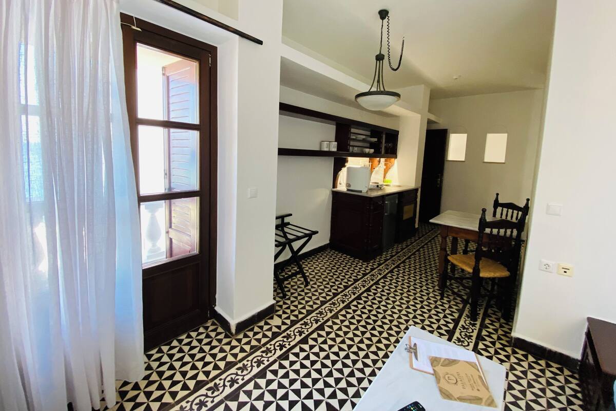 A room with a kitchen area, a dining table with chairs, and a patterned floor.