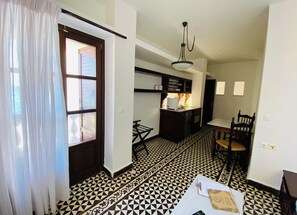 Una habitación con piso a cuadros blanco y negro, una puerta de madera, una mesa blanca con un portapapeles y una silla.