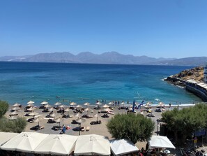 Une plage avec des parasols et des chaises longues, une côte rocheuse et des montagnes en arrière-plan.