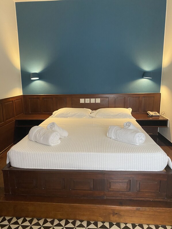 A neatly made bed with white linens and towels, a wooden headboard, and two wall-mounted light fixtures.