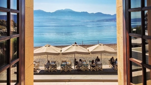 Un espace extérieur aménagé avec des tables et des parasols, offrant une vue sur un plan d’eau et des montagnes.