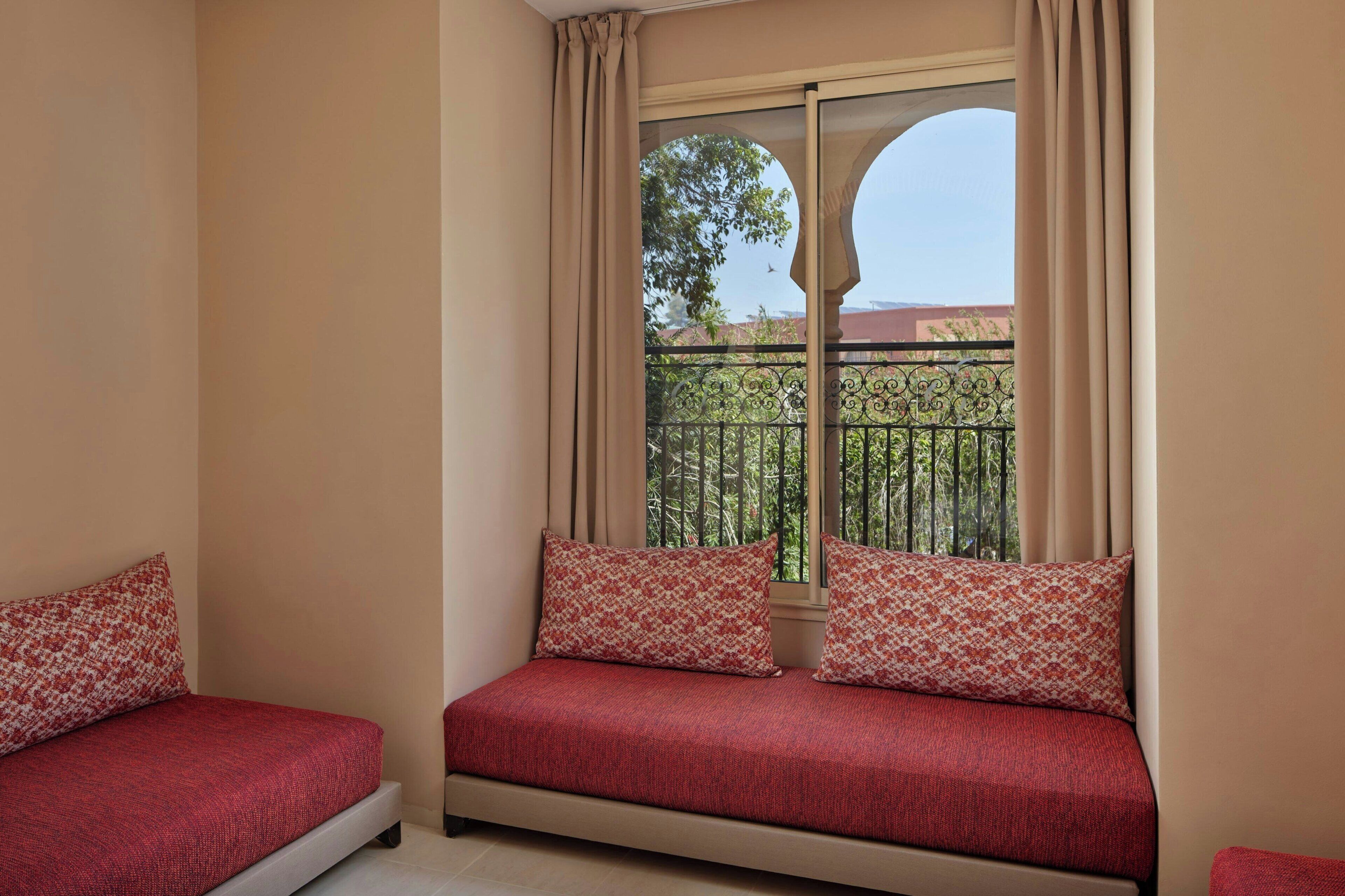 Une chambre avec deux lits simples, une fenêtre avec des rideaux et une vue sur un balcon doté d’une balustrade.