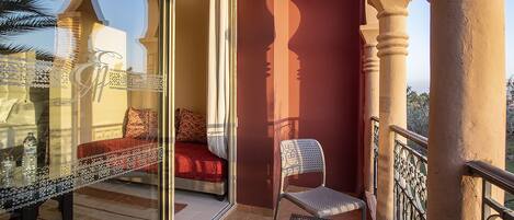 A balcony with a glass door, a red sofa, a white chair, and a small table.