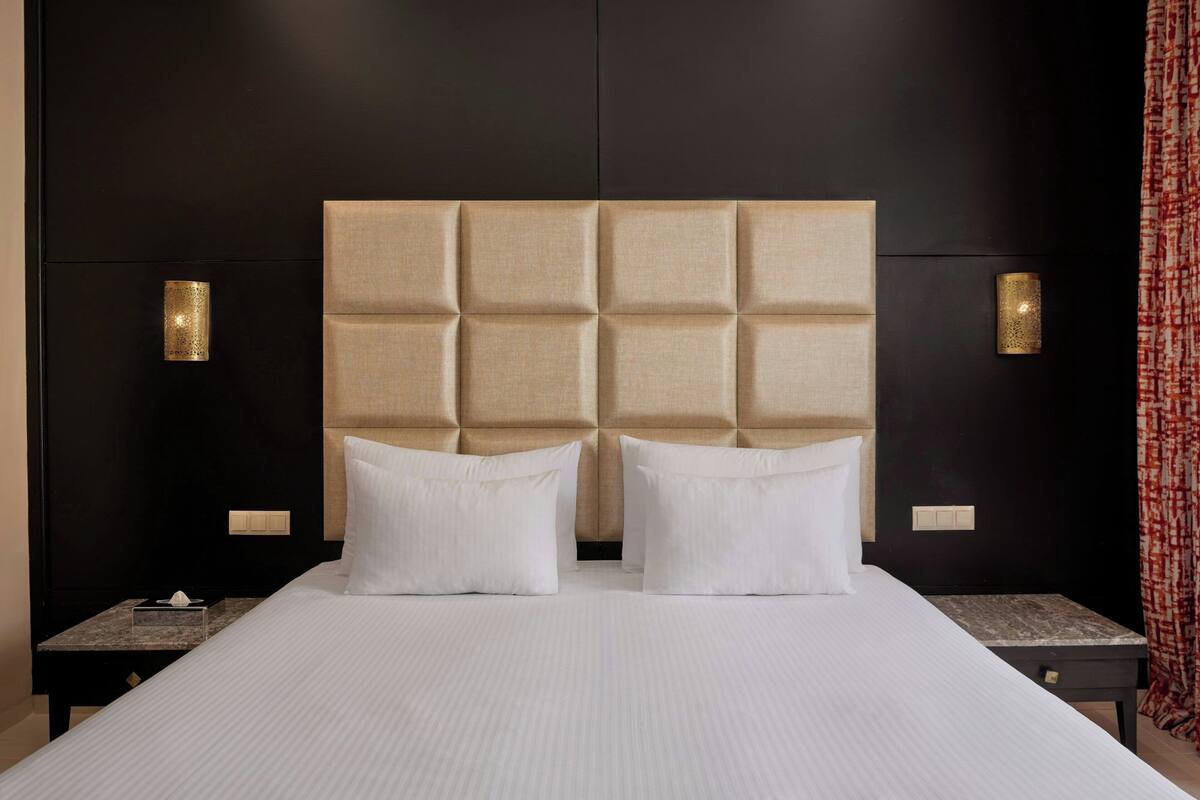 Une chambre d’hôtel avec un grand lit, deux tables de chevet et un mur sombre agrémenté de deux appliques murales.